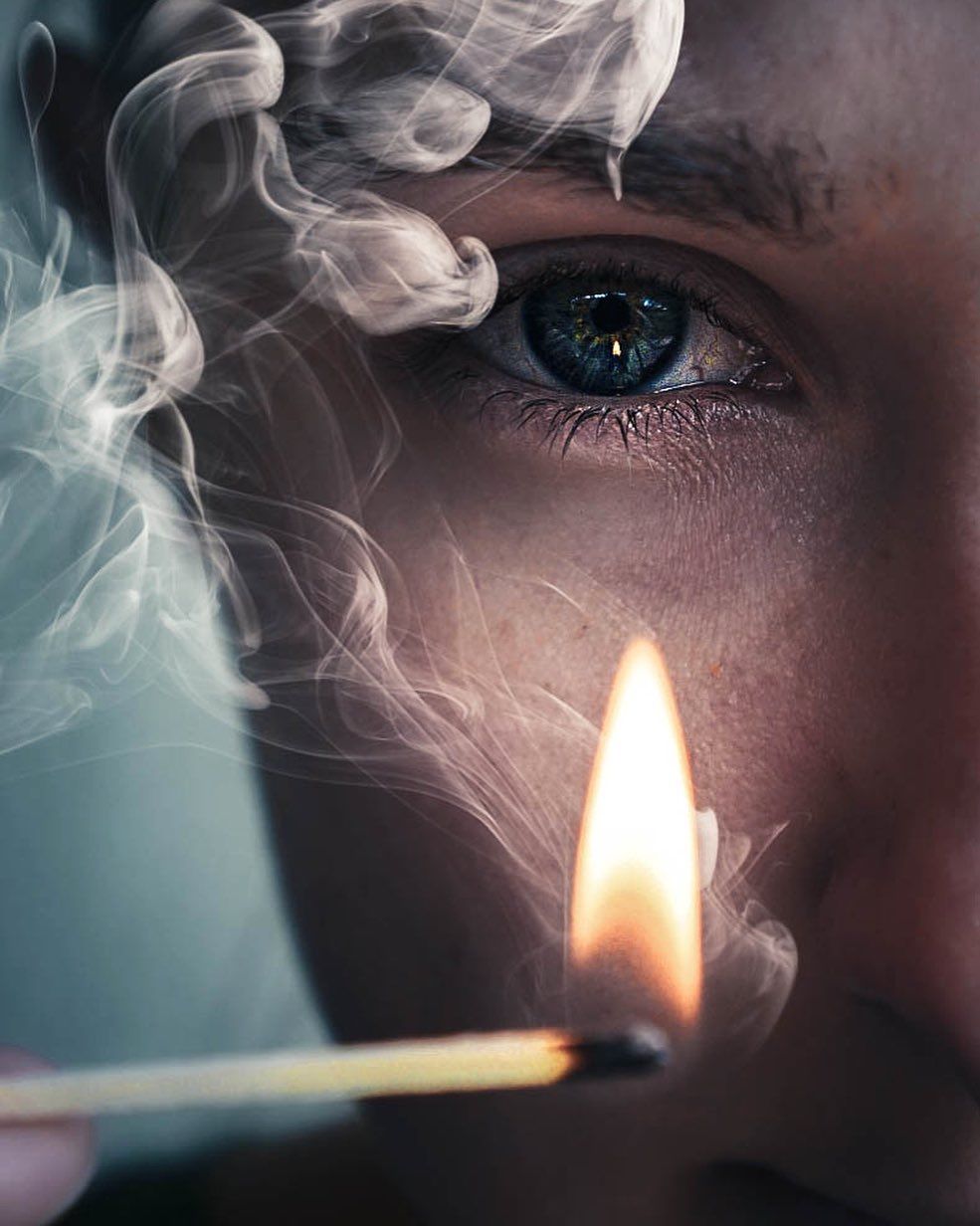 A photo of someone holding a lit matchstick infront of their eye.